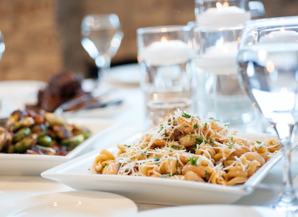 Pasta topped with cheese at a table with water glasses at an event catered by Green Mill Catering